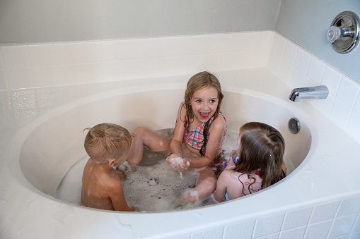 Cute elementary age kids take a bath while wearing swimsuits in bathroom