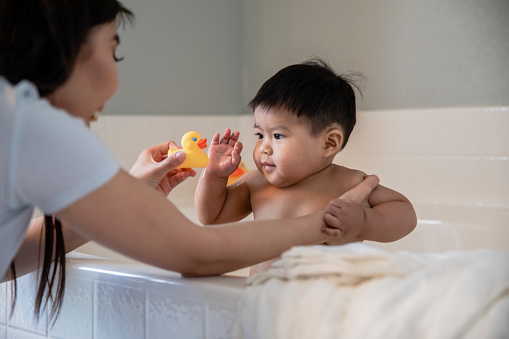 Adorable baby boy plays with rubber duck while his mother gives him a bubble bath