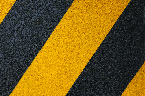 Texture and background. The concrete wall is painted diagonally in yellow and black stripes. Concept image for caution and warning, danger and hazard.