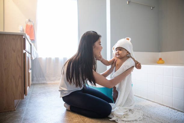 il bambino tocca la faccia delle madri mentre lei lo avvolge in un asciugamano dopo un bagno di bolle in bagno - bathtub child bathroom baby foto e immagini stock