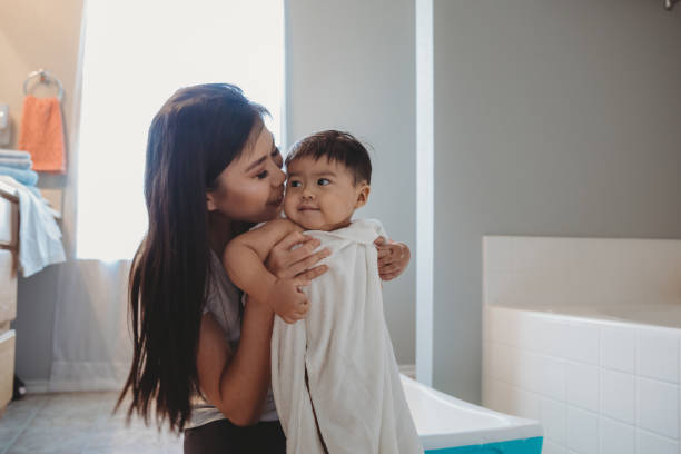 la madre coccola il bambino mentre lo avvolge in asciugamano dopo il suo bagno di bolle - bathtub child bathroom baby foto e immagini stock