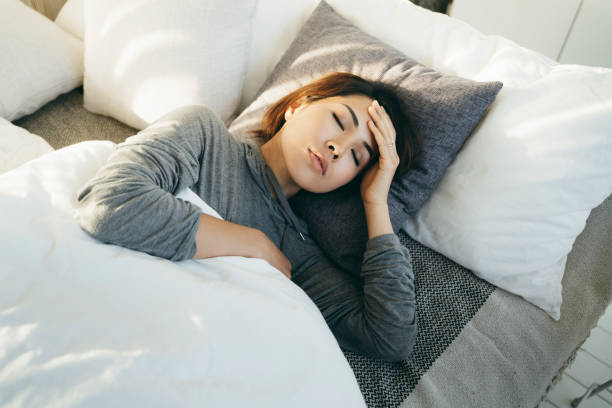 Young Asian woman with hand on forehead lying in bed and feeling sick Young Asian woman with hand on forehead lying in bed and feeling sick hospital depression sadness bed stock pictures, royalty-free photos & images