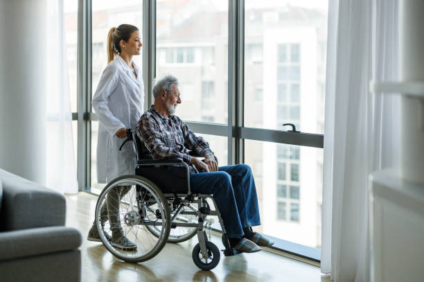 disabled mature man and his caregiver looking through window at home. - wheelchair disabled senior adult female nurse imagens e fotografias de stock