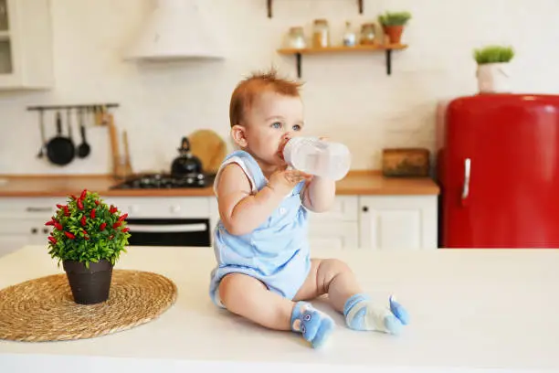 babyboy sitting on the table in the kitchen and drinking from baby bottle