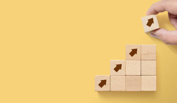 Hand arranging wood block stacking as step stair on paper yellow background with copy space. Ladder career path concept for business growth success process