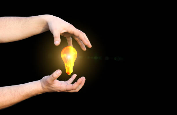 istock Man's hands holding lamp bulb. Electricity usage concept. Isolated on black background. 1257150062