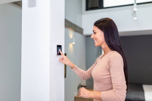 istock Woman using smart wall home control system in modern apartment. woman touching the display and controlling smart home system hanging on the wall in her apartment 1257153981