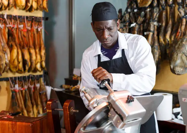 Photo of Seller slicing ham on slicer machine