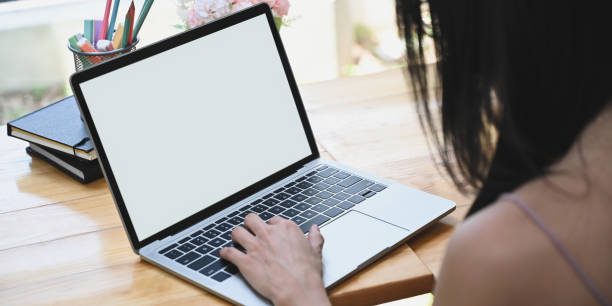 istock Cropped image woman is using a white blank screen computer laptop at the wooden working desk. 1257158423