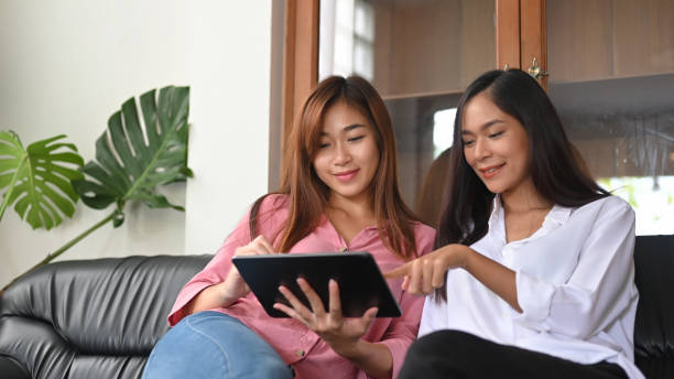 istock Women are relaxing with a computer tablet while sitting together on a black leather sofa. 1257158555