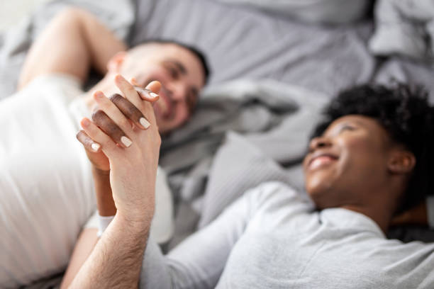 istock Young multiethnic couple holding hands while lying in bed in morning 1257163407