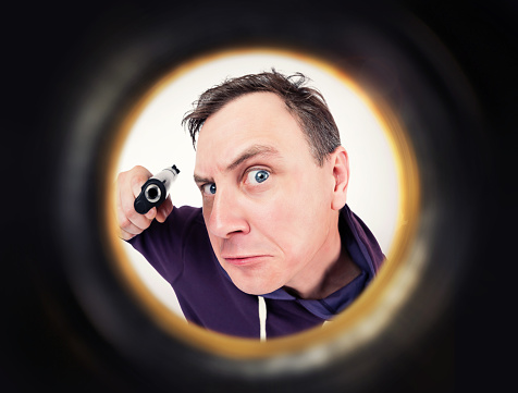 Man with a gun is seen through the peephole. Crime protection concept.