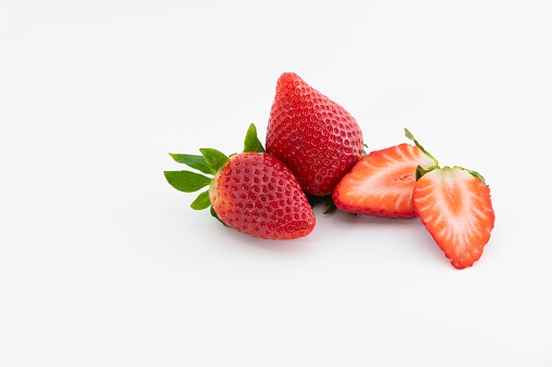 Close up two fresh whole strawberries next to a strawberry cut in half on a light background. Healthy and vegan food concept.