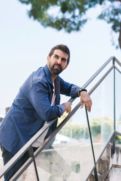 istock Bearded man leaning on fence while looking away 1257165138