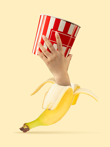 Banana hand holding big bucket of popcorn on yellow background. Fresh look. Copyspace to insert your text. Modern design. Contemporary artwork, collage. Concept of inspiration, creativity, artwork.