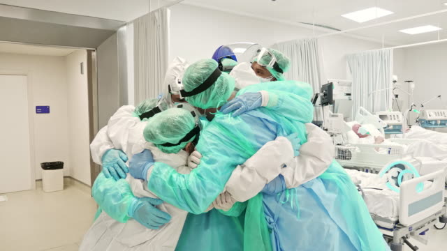 Real time video of healthcare workers in full protective wear standing together in group embrace in ICU.
