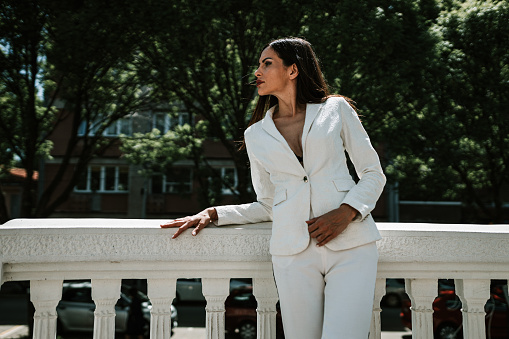 Beautiful young fashionable woman wearing a white suit standing on the balcony outdoors