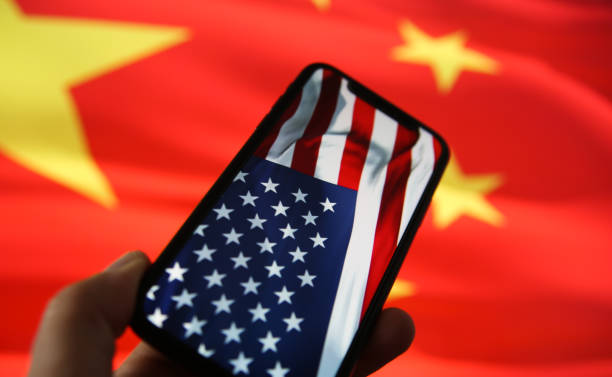 chinese american economic relationship concept: view on hand holding mobile phone with usa flag. blurred flag of china background - war criminal imagens e fotografias de stock