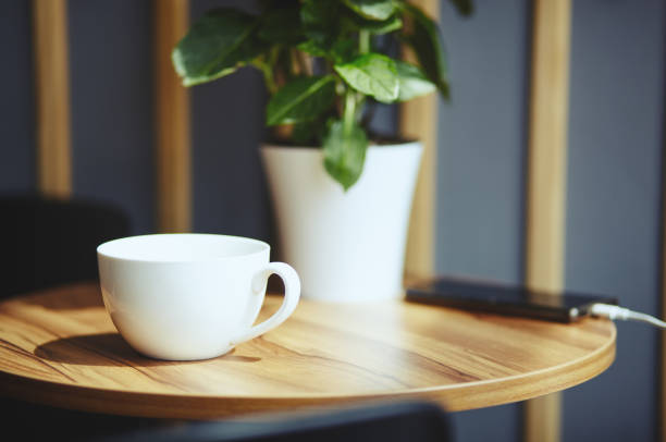 istock Empty white cup and smart phone on table in cafe. Morning light falls from the window.Coffee break.Blurred image,selective focus 1257170680