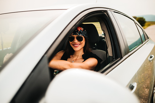 Young smiling woman driving with a guitar in a car and enjoying a summer road trip