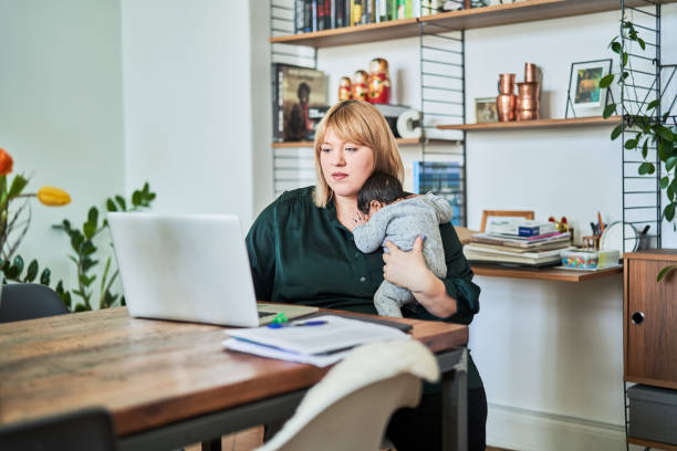 Mother with newborn working at home Single mother working at home while carrying baby. Confident woman using laptop in living room. She is multi-tasking. leanincollection stock pictures, royalty-free photos & images