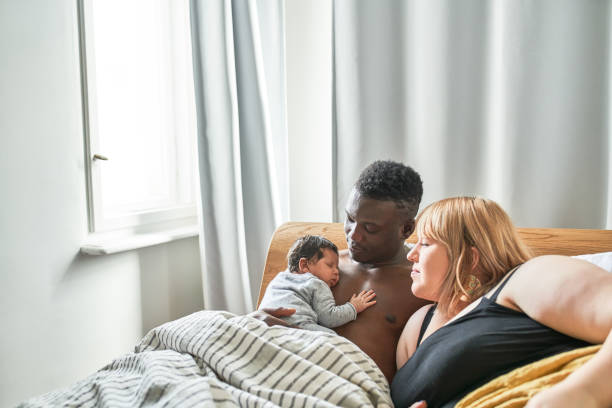 Smiling father and mother looking at baby in bedroom Shirtless father carrying newborn on bed. Mother is looking at baby in bedroom. They are smiling. biracial newborn stock pictures, royalty-free photos & images