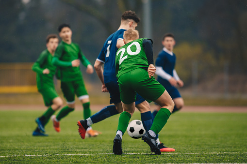 Soccer football players competing for ball and kick ball during match in the stadium on a rainy day. Footballers in action on the tournament game. Youth football competition