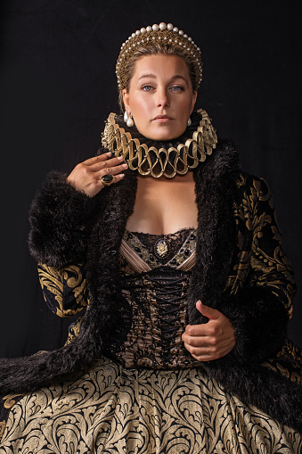 Portrait of a beautiful historical blonde Queen character wearing a period dress in a studio shot