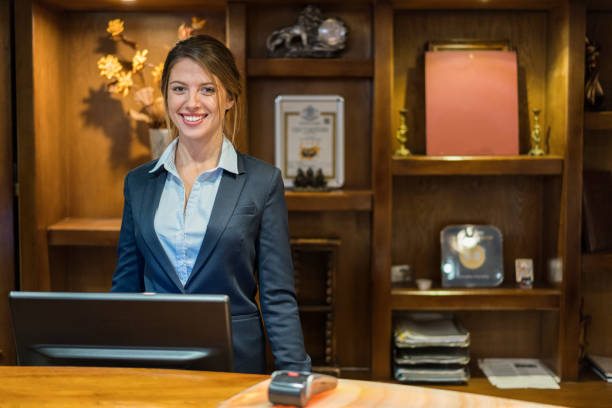 Hotel receptionist smiling at camera Portrait of smiling hotel receptionist standing at her workplace reception desk photos stock pictures, royalty-free photos & images