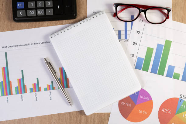 istock Blank notepad with financial graphs, eyeglasses, pen and calculator on the workplace. Top view. 1257189245