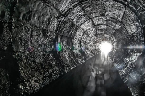 istock Round drainage concrete tunnel with water built with formwork. With light at the end. Underground river hidden in tube. 1257190440