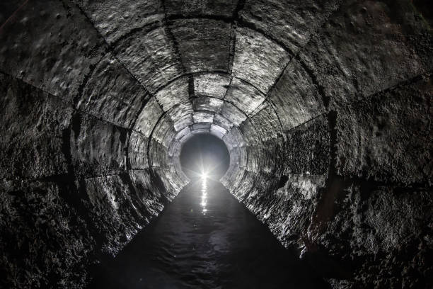 istock Round drainage concrete tunnel with water built with formwork. With light at the end. Underground river hidden in tube. 1257190464