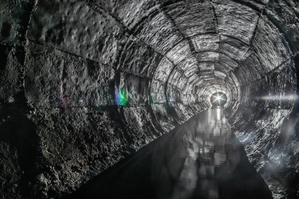 istock Round drainage concrete tunnel with water built with formwork. With a lantern light at the end. Underground river hidden in tube. 1257190478