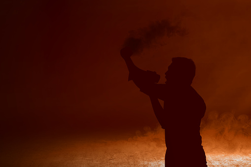 Silhouette of a man using a megaphone and holding flare doing protest with smoke background