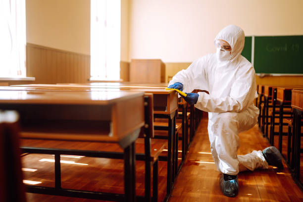 Man in a protective suit washes school desk.