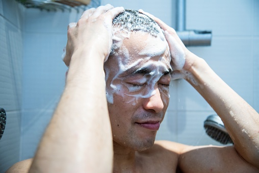 An East Asian man in his 30s taking a shower at home.