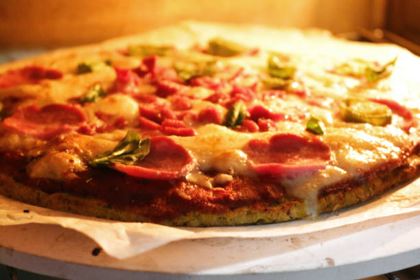 istock Image of cooked homemade cauliflower base pizza baking in oven, cooked on pizza stone for thin and crispy base, pepperoni and fresh basil leaves on top 1257209738