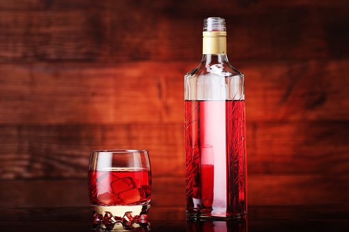 bottle of flavored vodka with a glass on a wooden background