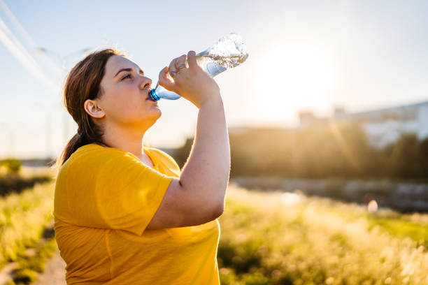 donna oversize che beve acqua dopo la corsa - adult jogging running motivation foto e immagini stock