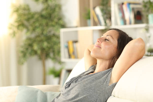 femme adulte heureux détendant dans le sofa à la maison - respiration femme maison photos et images de collection