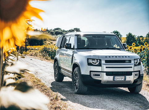 Siena, Italy - July 12, 2020 : The New Land Rover Defender 2020 is parked on the countryside with a field of sunflowers in the background