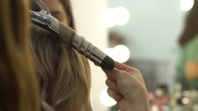 Close-up view of stylist hairdresser making hairstyle using curling tongs.
