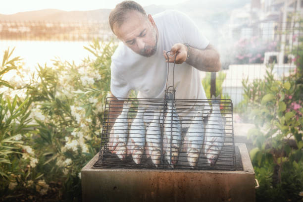 middle aged man is cooking fish at barbecue
