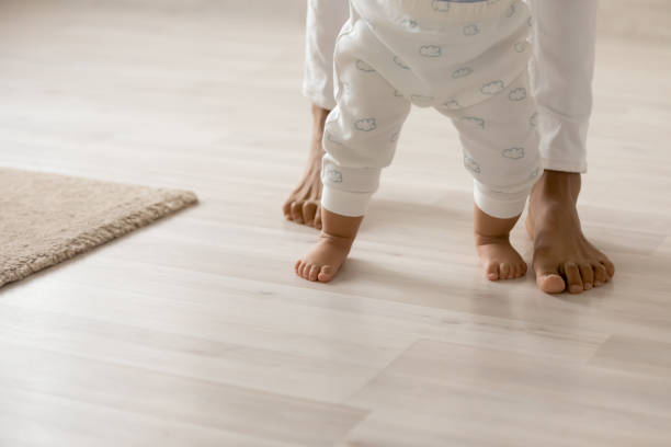 Close up barefoot African American woman with toddler child standing Close up barefoot African American woman with toddler child standing on warm wooden floor with underfloor heating, caring loving young mum teaching adorable little daughter to walk at home young hot stock pictures, royalty-free photos & images