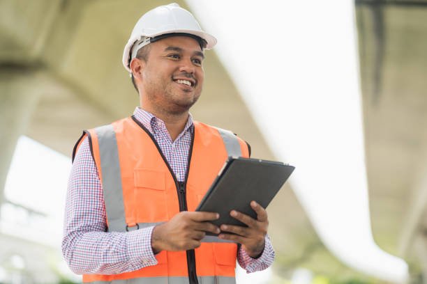 istock Asian civil engineer operate with tablet to control working at construction. Worker wearing hard hat at highway concrete road site. 1257231266