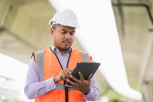 istock Asian civil engineer operate with tablet to control working at construction. Worker wearing hard hat at highway concrete road site. 1257231752