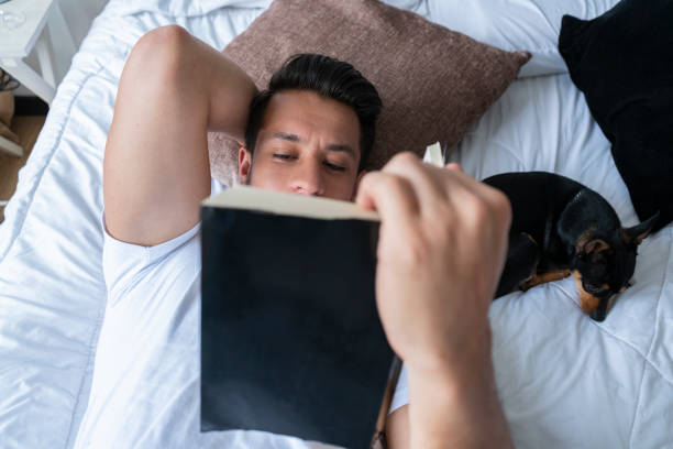 istock Latino ethnic man lying in bed reading a book with his dog during Covid-19 1257237607