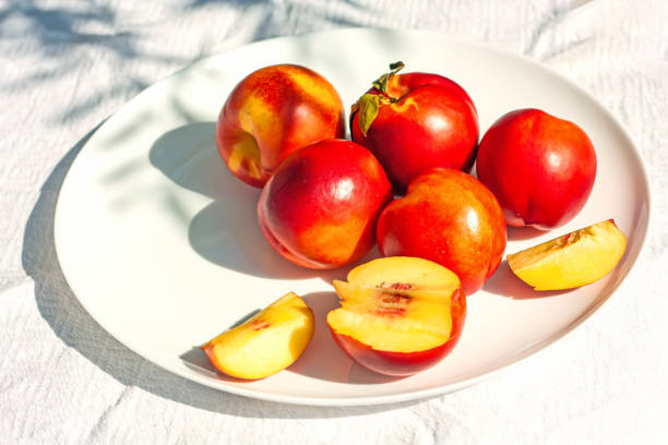 frutas de nectarina orgânica maduras vermelhas na placa branca no fundo da natureza. conceito de alimentação saudável no verão. antioxidante de frutas. foco seletivo - zeaxanthin - fotografias e filmes do acervo