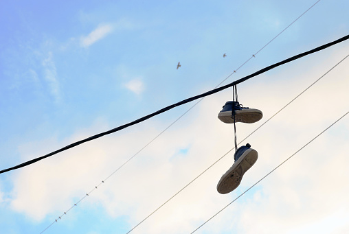 Sports shoes dangling on power cable. Pair of old sneakers hanging on electric wires