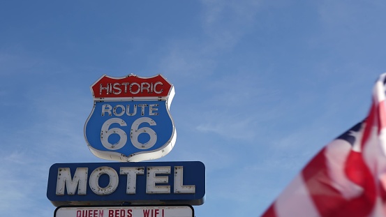 Motel retro sign on historic route 66 famous travel destination, vintage symbol of road trip in USA. Iconic lodging signboard in Arizona desert. Old-fashioned neon signage. National state flag waving.
